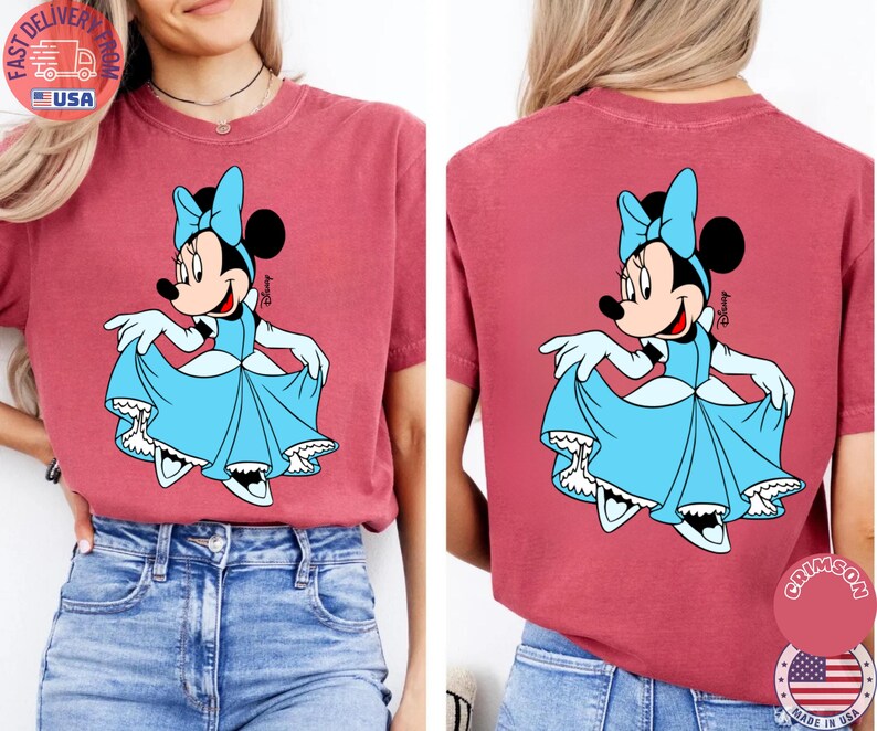 May include: A red-pink t-shirt featuring a Minnie Mouse graphic in a light blue dress and bow. The front and back of the shirt display the same design. The shirt has short sleeves and a relaxed fit. The shirt has a round neck.