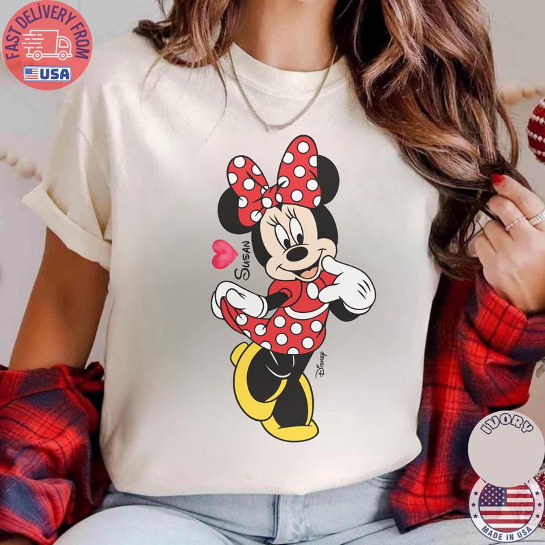 May include: Cream-coloured t-shirt with a Minnie Mouse graphic. Minnie is shown in a red dress with white polka dots, a matching bow, and yellow shoes. The name "Susan" is written on the graphic.