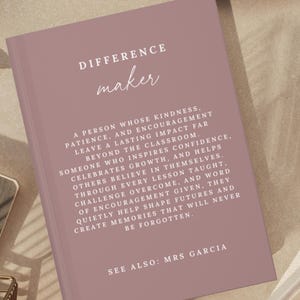 May include: A mauve-coloured book with white text on the cover. The text reads: DIFFERENCE maker. A PERSON WHOSE KINDNESS, PATIENCE, AND ENCOURAGEMENT LEAVE A LASTING IMPACT FAR BEYOND THE CLASSROOM. SEE ALSO: MRS GARCIA. The book has a matte finish.