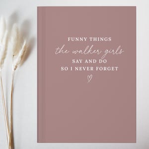 May include: A dusty rose coloured journal with white text that reads: FUNNY THINGS the walker girls SAY AND DO SO I NEVER FORGET, followed by a small hand-drawn heart outline centred at the bottom of the front cover.