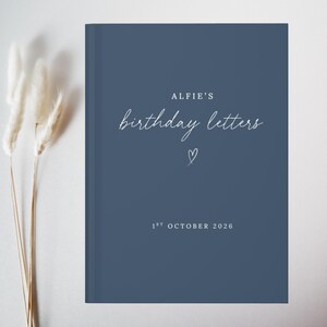 May include: A dark blue hardcover book with white text that reads ALFIE'S birthday letters, a small hand-drawn heart, and the date 1ST OCTOBER 2026. The book cover features a clean, solid matte finish with centered typography and a simple heart icon.
