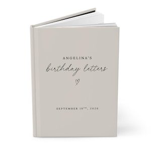 May include: A light beige hardcover book with white pages visible at the top. The cover features black text reading ANGELINA'S birthday letters, a small hand-drawn heart icon, and the date SEPTEMBER 19TH, 2026 printed in a clean, minimalist font.