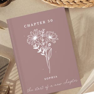 May include: A dusty rose hardback book featuring a white line art illustration of a floral bouquet. The text reads "CHAPTER 30" at the top, "SOPHIA" in the centre, and "the start of a new chapter" in a cursive script at the bottom.