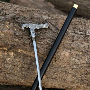 May include: A white ceramic mug with a black handle and the text "But First, Coffee" in a black, handwritten-style font. The mug is on a white surface.