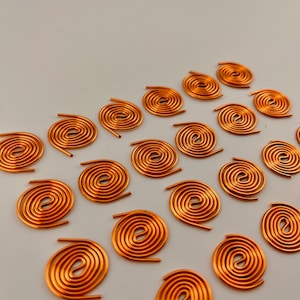 May include: Copper wire spirals arranged on a white surface. Each spiral is a warm, reddish-orange color, with a circular design and straight wire ends. The coils are evenly spaced, creating a pattern.