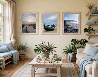 May include: Three rectangular framed wall art prints featuring coastal scenes: a sandy beach path at sunset, a blue and green fishing boat on the sand labeled NAZARE, and a rocky shoreline. The prints are displayed in light wood frames.