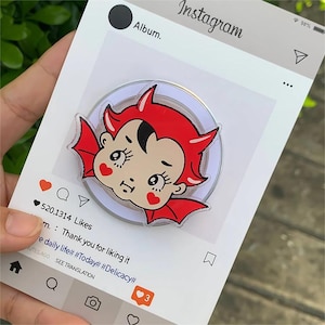 May include: A cartoon devil pin with red horns and wings, set against a white background with an Instagram-style layout. The layout includes a heart icon and the word "Instagram".