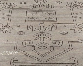 May include: A light beige rug with a geometric pattern in dark brown. The rug features a central design with floral and geometric shapes. The text "JP RUGSS" is visible in the lower left corner. The rug is made of a woven material.