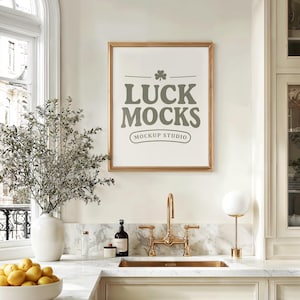 Puede incluir: Una impresión enmarcada con el texto "LUCK MOCKS MOCKUP STUDIO" en un entorno de cocina. La impresión está encima de un grifo y un fregadero dorados. Un jarrón blanco con vegetación y un cuenco de limones están en la encimera.