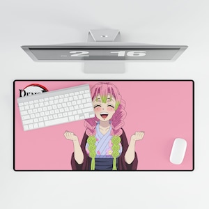 Op de afbeelding: Een roze rechthoekige muismat met een lachend anime-personage met roze haar en groene accenten. Een wit toetsenbord en muis liggen op de mat. Het Demon Slayer-logo staat in de linkerbovenhoek.