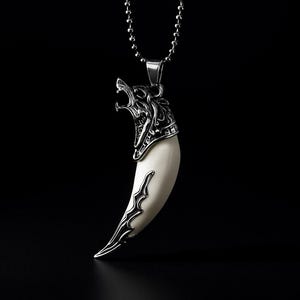 May include: A silver-colored pendant necklace featuring a stylized wolf head biting a large, off-white tooth. The pendant hangs from a ball chain necklace against a black background. The wolf head has intricate details.