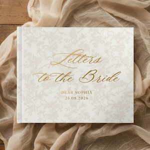 Pode incluir: Um livro retangular de capa dura com uma capa branca apresentando um padrão floral rosa claro suave. O texto dourado na frente diz Letters to the Bride, DEAR SOPHIA e 25.08.2026 em uma combinação de escrita elegante e letras de forma.