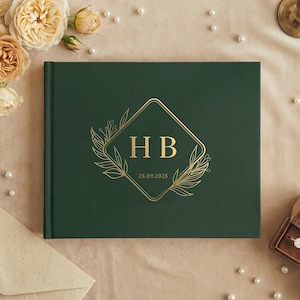 May include: A dark green wedding guest book with gold foil lettering. The cover features the initials "HB" inside a diamond shape, surrounded by floral elements. The date "25.09.2025" is also displayed. The book is surrounded by pearls and flowers.