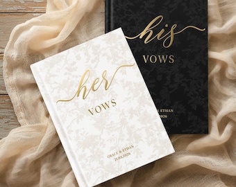 May include: Two hardback vow books featuring floral patterns. One book is white with gold text reading "her VOWS" and "GRACE & ETHAN 21.03.2026". The other is black with gold text reading "his VOWS" and "GRACE & ETHAN 21.03.2026". Both feature elegant script lettering.