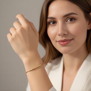 Può includere: Un braccialetto dorato con un design lineare con piccole perle distanziate in modo uniforme. Il braccialetto è indossato su un polso, mostrando la sua estetica semplice ma elegante. Il gioiello è un accessorio delicato.