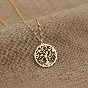 May include: A gold-colored necklace with a pendant featuring a tree of life design. The pendant is circular with intricate cut-out details of the tree's branches and roots. The necklace chain is delicate and gold-toned.