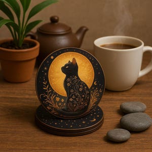 May include: Round black cat coasters with a golden moon and floral design. The black cat is silhouetted against the moon. The coasters are stacked on a wooden surface, with a cup of coffee and a teapot in the background.