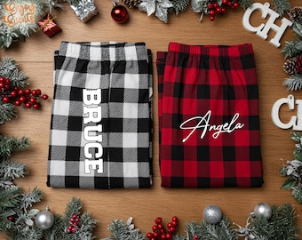May include: Two pairs of personalized pajama pants. One pair is black and white buffalo plaid with the name "Bruce" in white. The other pair is red and black buffalo plaid with the name "Angela" in white.