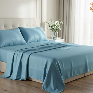 May include: A light blue bed linen set on a bed, comprising a fitted sheet, a flat sheet, and two pillowcases. The bedding is neatly arranged, with soft folds and a smooth texture. The scene is set in a bedroom with a neutral colour palette.