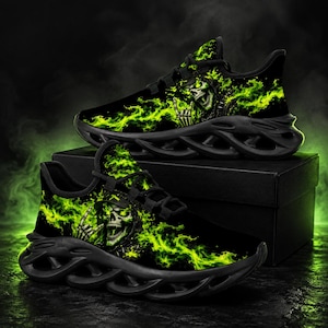 Puede incluir: Un par de zapatillas deportivas negras con un patrón de llamas verde brillante y un gráfico de una calavera con gorra haciendo un gesto con la mano. Los zapatos tienen cordones negros y una suela negra gruesa y esculpida.
