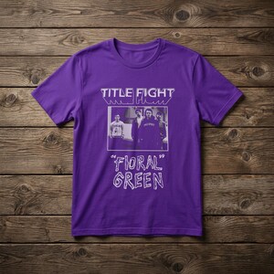 Puede incluir: Una camiseta morada de manga corta con un estampado gr&aacute;fico en blanco. El dise&ntilde;o incluye el texto "TITLE FIGHT" en la parte superior, una fotograf&iacute;a rectangular en blanco y negro de cuatro personas en el centro y el texto "FLORAL GREEN" debajo.