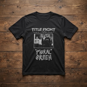 Puede incluir: Una camiseta negra de manga corta con un estampado gr&aacute;fico en blanco. El dise&ntilde;o incluye el texto "TITLE FIGHT" en la parte superior, una fotograf&iacute;a en blanco y negro de cuatro personas en el centro y el texto "FLORAL GREEN" en una fuente estilizada.