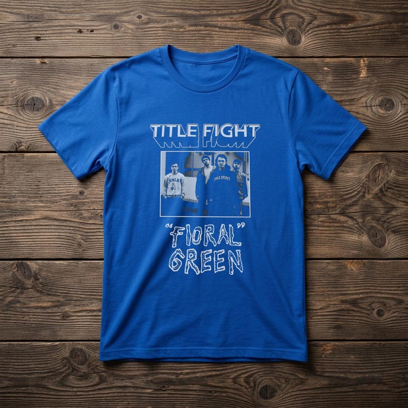 Puede incluir: Una camiseta azul brillante de manga corta con un estampado gr&aacute;fico blanco. El dise&ntilde;o incluye el texto "TITLE FIGHT" en la parte superior, una fotograf&iacute;a rectangular de cuatro personas en el centro y el texto "FLORAL GREEN" en una fuente estilizada.