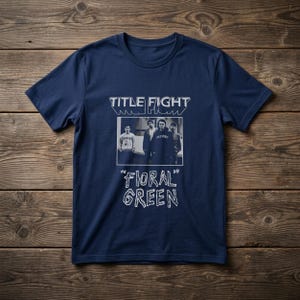 Puede incluir: Una camiseta de manga corta color azul marino con un estampado gr&aacute;fico en blanco. El dise&ntilde;o incluye el texto "TITLE FIGHT" en la parte superior, una fotograf&iacute;a en blanco y negro de cuatro personas en el centro y "FLORAL GREEN" abajo.