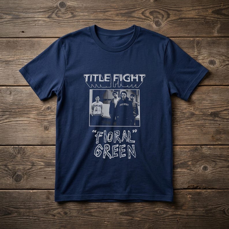 Puede incluir: Una camiseta de manga corta color azul marino con un estampado gr&aacute;fico en blanco. El dise&ntilde;o incluye el texto "TITLE FIGHT" en la parte superior, una fotograf&iacute;a en blanco y negro de cuatro personas en el centro y "FLORAL GREEN" abajo.
