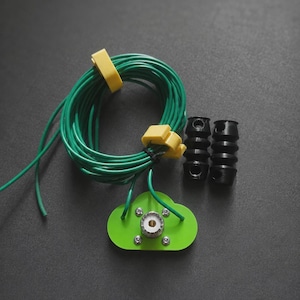 May include: A green cloud-shaped antenna mount with a central silver connector, attached to a coiled green wire secured by two yellow clips. Two black, ribbed cylindrical components are positioned to the right of the antenna assembly.