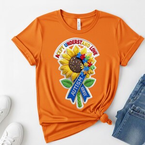 May include: Orange t-shirt featuring a sunflower design with the words "Accept, Understand, Love" and a blue ribbon that says "Autism". The sunflower has a brown center and colorful puzzle pieces.