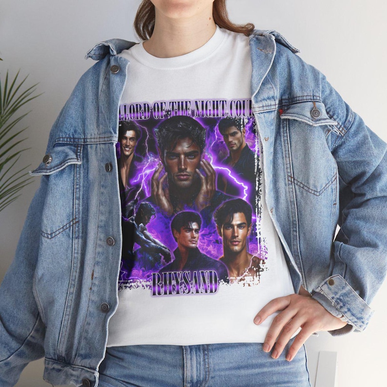 May include: White t-shirt featuring a graphic design with the text "LORD OF THE NIGHT COURT" and "RHYSAND". The design includes multiple images of a man with purple lightning effects. The person is wearing a light blue denim jacket.