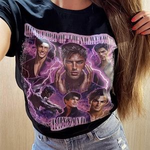 May include: Black t-shirt featuring a graphic design with the text "HIGH LORD OF THE NIGHT COURT" and the name "RHYSAND". The design includes portraits of several men with purple lightning effects.