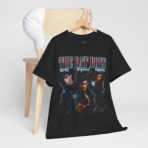 May include: Black t-shirt featuring the text "THE BAT BOYS" in a retro font, with the names Azriel, Rhysand, and Cassian below. The shirt displays a graphic of three men in dark clothing.