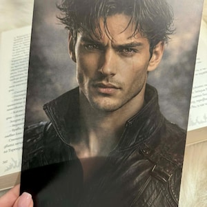 May include: A rectangular print featuring a portrait of a person with dark, wavy hair and brown eyes. The individual has a defined jawline and is wearing a dark brown leather jacket with a high collar and visible stitching details against a dark background.