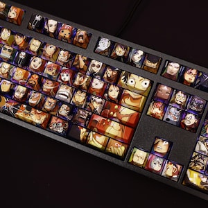 May include: A black computer keyboard with custom keycaps featuring colourful anime character illustrations. The keycaps display various faces and figures, creating a vibrant and detailed design. The keyboard is angled, showing the keycaps in detail.