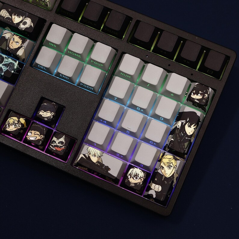 Op de afbeelding: Een zwart mechanisch toetsenbord met aangepaste keycaps met anime-personage-illustraties. De keycaps zijn wit en zwart, met kleurrijke LED-achtergrondverlichting. Het toetsenbord heeft een standaardindeling met functietoetsen en een numeriek toetsenbord.