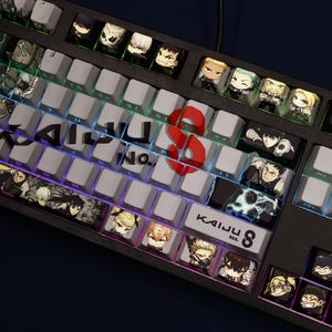 Op de afbeelding: Een zwart mechanisch toetsenbord met aangepaste keycaps met anime-karakterillustraties. Het toetsenbord heeft een rode "8"-toets en de tekst "KAIJU No. 8". De toetsen zijn verlicht met een regenboogverloop.