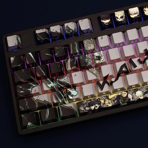 Op de afbeelding: Een zwart mechanisch toetsenbord met aangepaste keycaps met anime-achtige karakterkunst en abstracte ontwerpen. De keycaps zijn een mix van wit, zwart en grijs, met kleurrijke achtergrondverlichting zichtbaar.