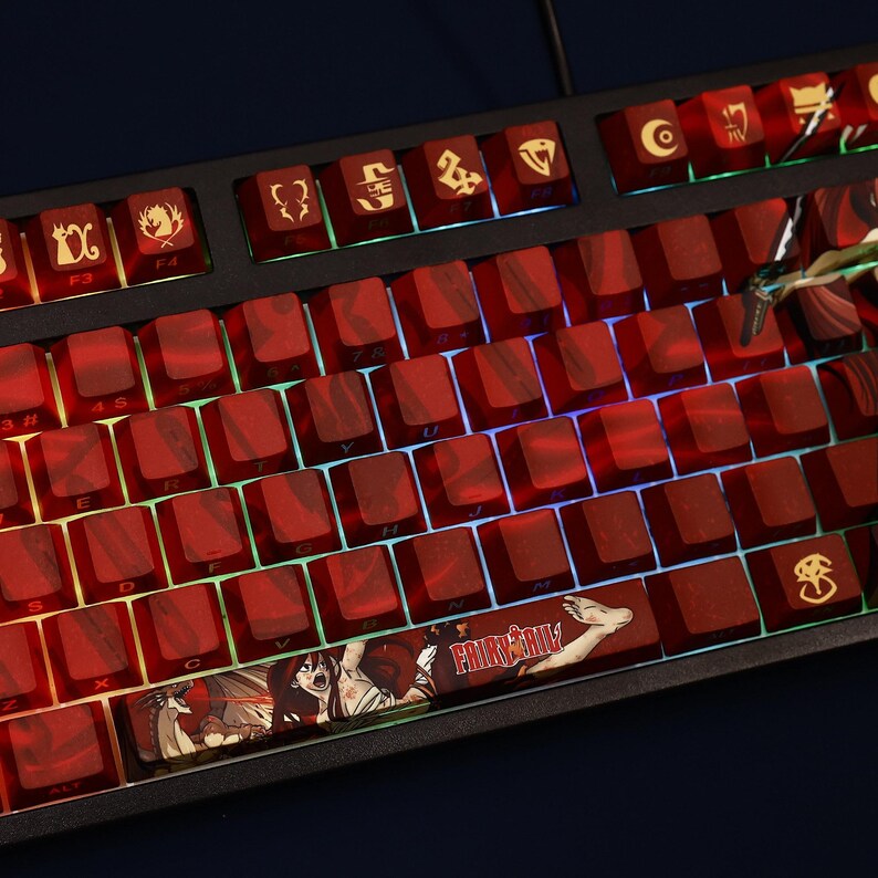 May include: A mechanical keyboard with red keycaps and a black frame. The keycaps have a marbled effect and feature custom designs and symbols. The space bar displays the text "FAIRY TAIL" with anime characters. The keyboard is lit with a colorful backlight.