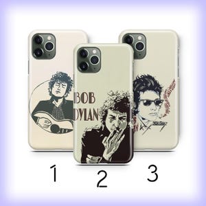 May include: Three phone cases with Bob Dylan graphics. The cases are off-white with black and sepia-toned illustrations of the musician. One case features Dylan playing guitar, another has the text "Bob Dylan", and the third shows him smoking.