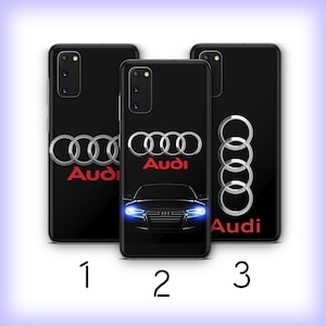 Puede incluir: Tres fundas negras para teléfono con el logotipo de Audi en plata y rojo. La funda central presenta una silueta de coche con faros azules. Las fundas están numeradas 1, 2 y 3.