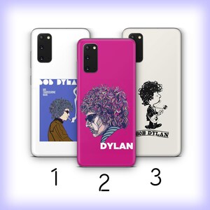 May include: Three phone cases featuring Bob Dylan artwork. The cases are white and magenta. One case has a blue and brown image of Dylan smoking. Another case is magenta with a Dylan portrait and the name "Dylan". The third case is white with a cartoon Dylan playing guitar.