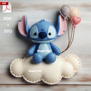 May include: A blue felt Stitch doll with large ears and a dark blue nose and eyes, sitting on a cream-colored felt cloud. Three felt balloons in gray, cream, and pink are attached. The text "Magix Felt" is visible on the cloud.