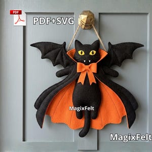 May include: A black felt cat wall hanging featuring bat wings, a bright orange cape lining, and an orange bow tie. The cat has yellow eyes and white fangs. The text PDF+SVG and MagixFelt are visible on the item. It hangs from a gold-colored hook.