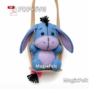Op de afbeelding: Een blauw vilten ezelknuffel met een paarse snuit en buik, zittend in een bruine schommel. De ezel heeft zwart haar en een zwarte staart met een roze accent. De tekst "PDF+SVG" en "MagixFelt" zijn zichtbaar.