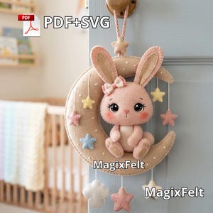 May include: A felt baby mobile featuring a pink bunny sitting on a crescent moon. The mobile includes hanging stars and clouds in pastel colors. The text "MagixFelt" is visible. The mobile is hanging on a light blue door.