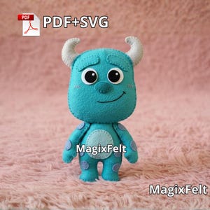 Puede incluir: Una muñeca monstruo de fieltro turquesa con ojos negros grandes, cuernos pequeños y una cara sonriente. La muñeca tiene manchas moradas y una barriga azul claro. El texto "MagixFelt" es visible en la muñeca y en la parte inferior. La imagen también incluye el texto "PDF+SVG".