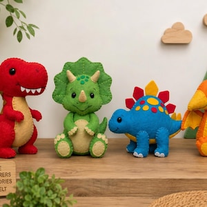 Puede incluir: Un conjunto de cuatro peluches de dinosaurio de fieltro que incluye un T-Rex rojo, un Triceratops verde, un Estegosaurio azul y un Pterodáctilo naranja. El T-Rex rojo mide 30 cm de altura. Un letrero de madera muestra el texto LITTLE ADVENTURERS GREAT STORIES MAGIXFELT.