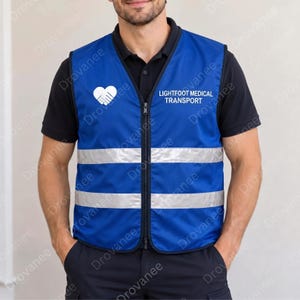 Può includere: Un gilet blu reale con cerniera frontale, due strisce riflettenti argentate orizzontali e un logo bianco a forma di cuore formato da due mani. Il testo LIGHTFOOT MEDICAL TRANSPORT è stampato in bianco sulla parte superiore del petto.